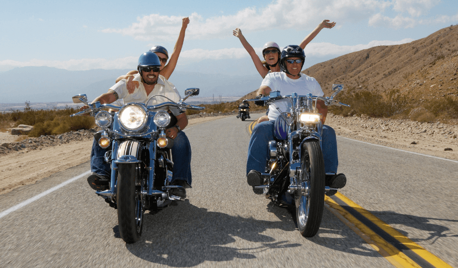 Two motorcyclists waving while riding on the road